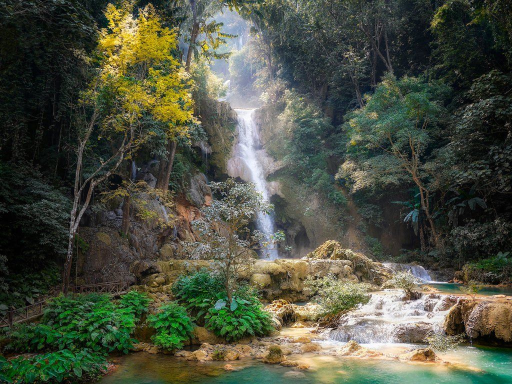 An idyllic & serene tropical waterfall rolls down the cliffs as it sits nestled between luscious trees.